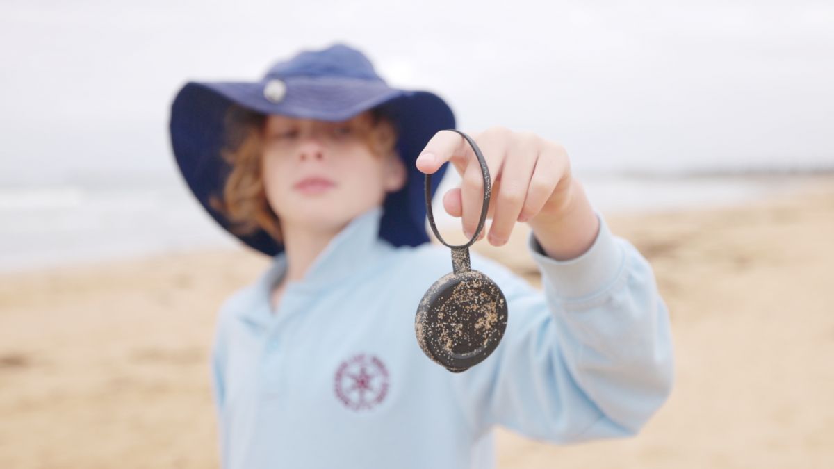 School kid holding plastic bottle cap on beach