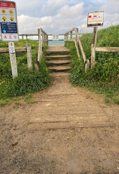 A dirt path with old and worn stairs leading to a beach.