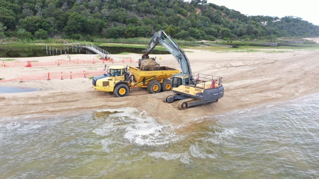 An excavator loading sand into a tip truck on the beach. 
