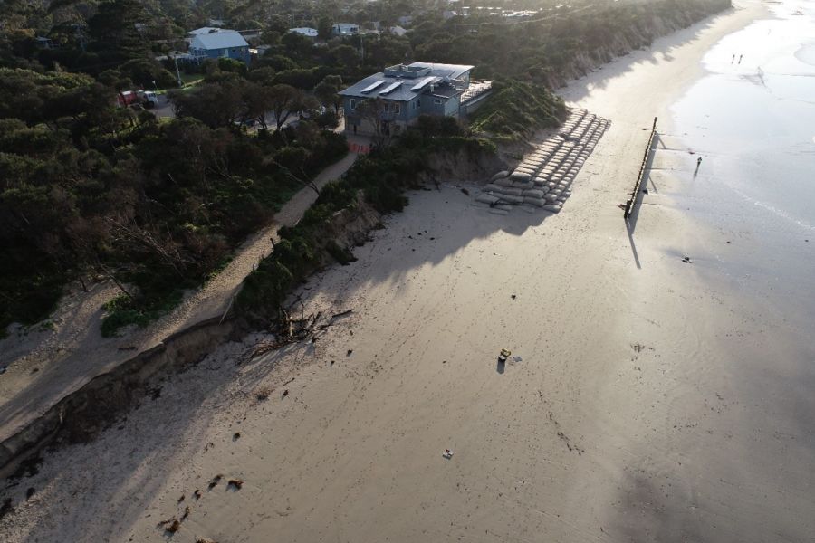 A drone image of an eroded beach with neat piles of sandbags on the beach in front of a building. 