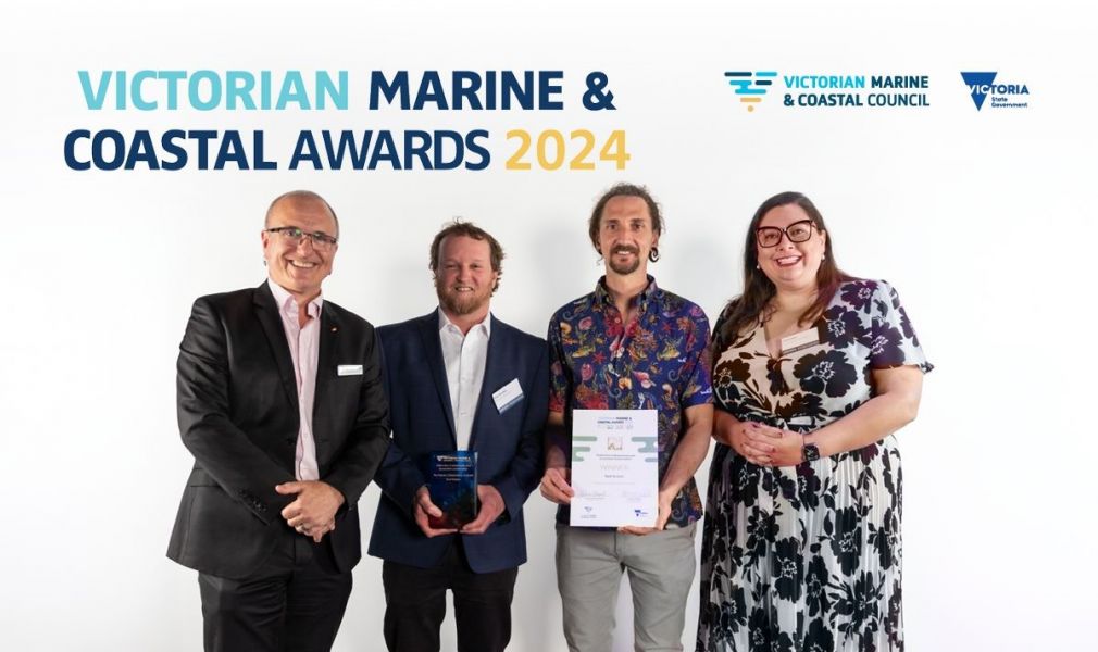 Four people posing for a photo. The Victorian Marine and Coastal Awards 2024 banner, VMaCC logo, and State of Victoria logo are included in the photo. 