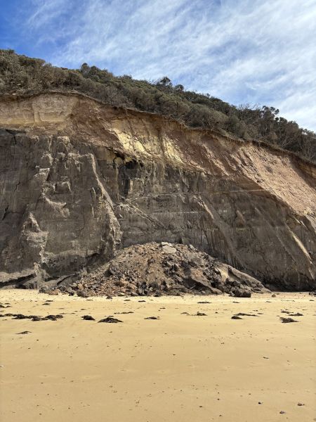 A close-up of a cliff with rubble at its base.