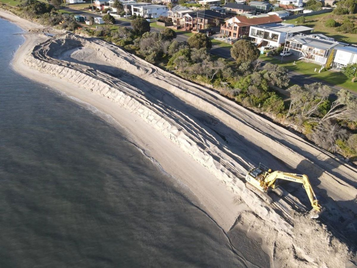 Ocean in the front, and sand bank wall. Houses in the distance