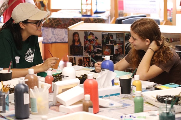 Two workshop participants looking and smiling at each other while exploring their seaweed art