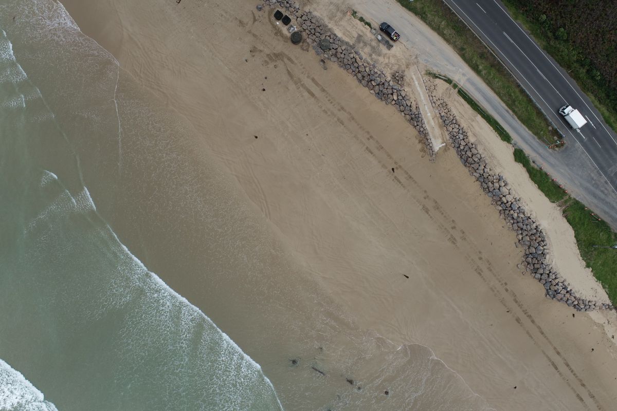 Eastern view of short term protection work. Aerial views. Sand and beach with a white truck on the road.