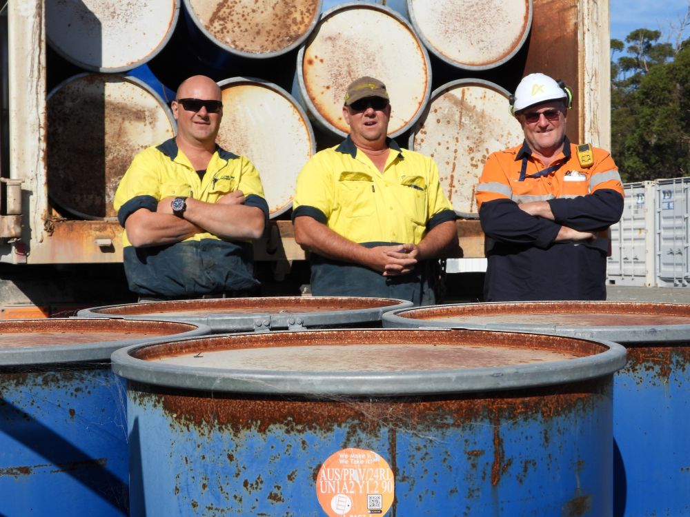 Three people standing in front of oil drums