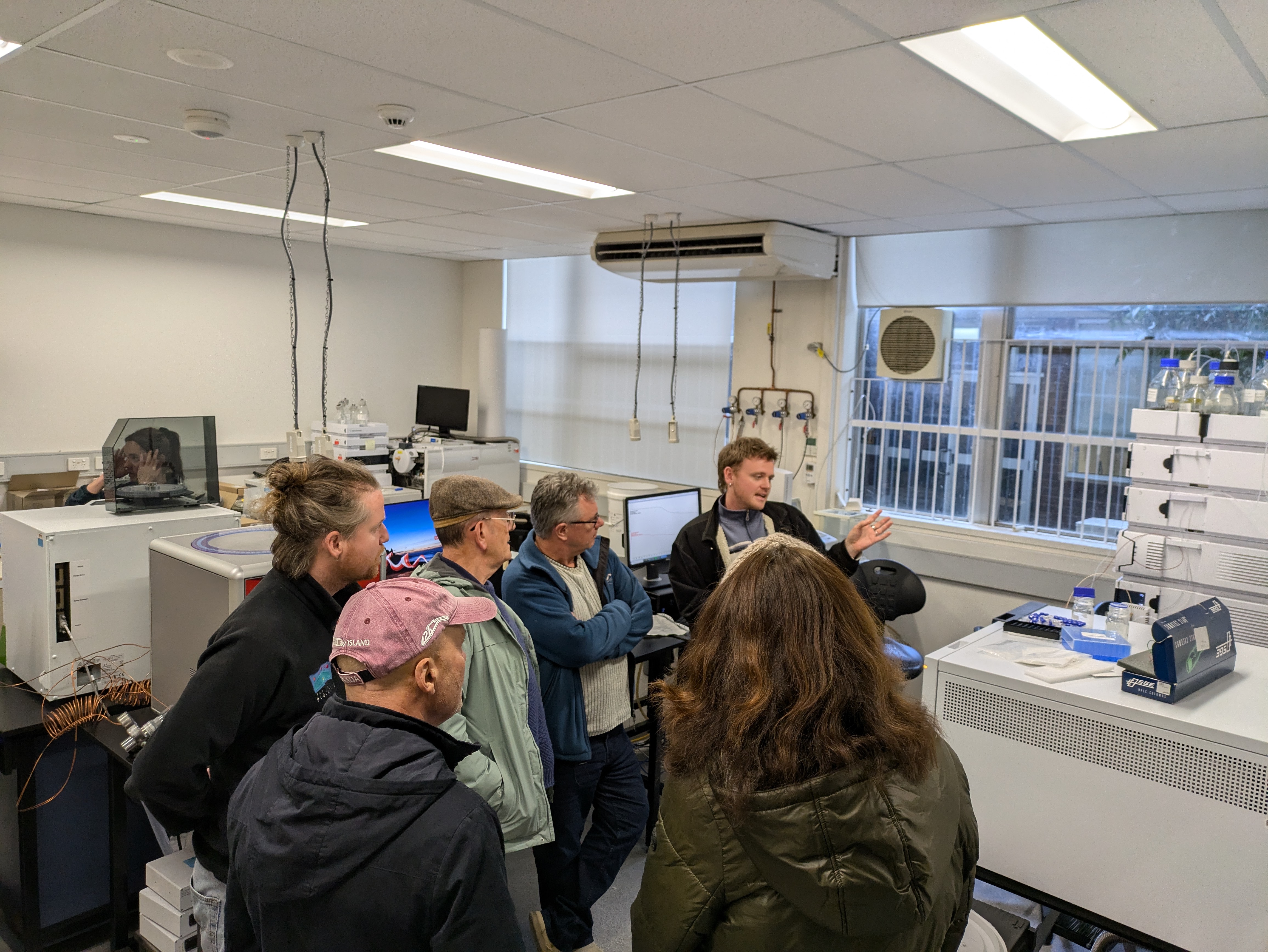 Six people gathered in a lab as 1 person is explaining the set up