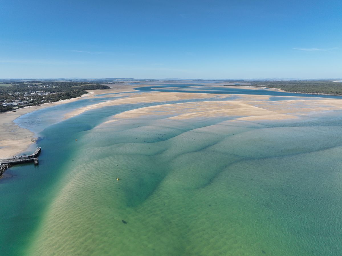 Aerial photo of a beach showing sandbanks, blue water and a pier